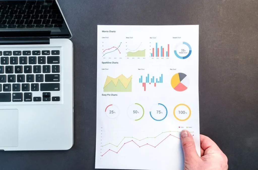Printed charts and graphs held beside a laptop