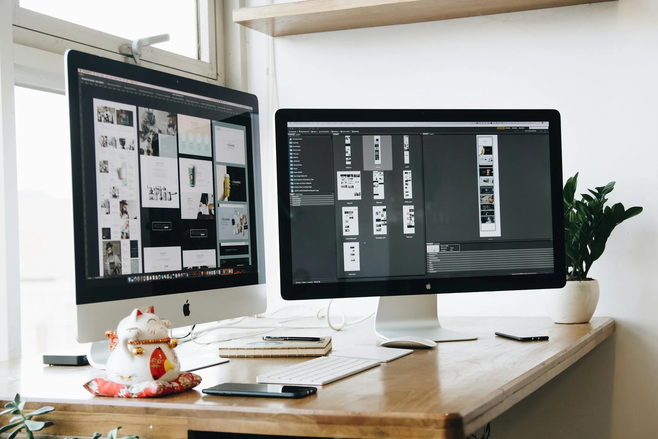 Two monitors showing website design work on a bright desk with a plant