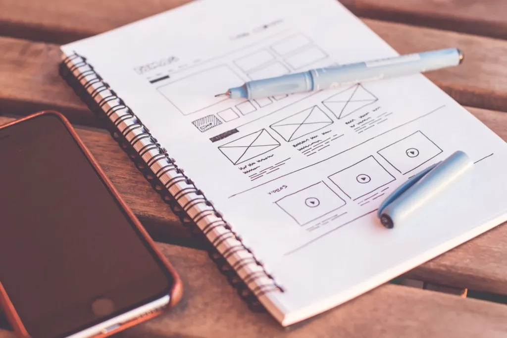 Website wireframe sketches in a notebook beside a smartphone